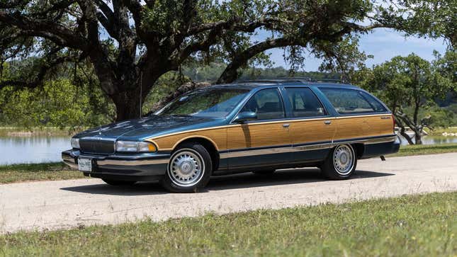 A photo of a dark blue 1996 Buick Roadmaster wagon with wood panels on the side parked in front of a lake