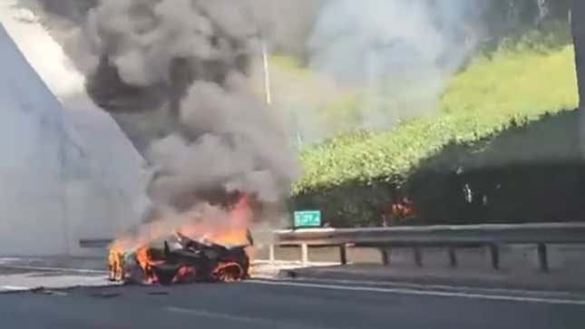 A screenshot showing a car on fire by the side of the road. 