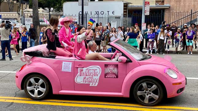 Ein rosa VW New Beetle Cabriolet mit darin sitzenden Menschen vor einer Menge