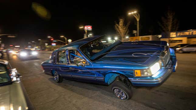 A dark blue Low Rider car drives on a street. 