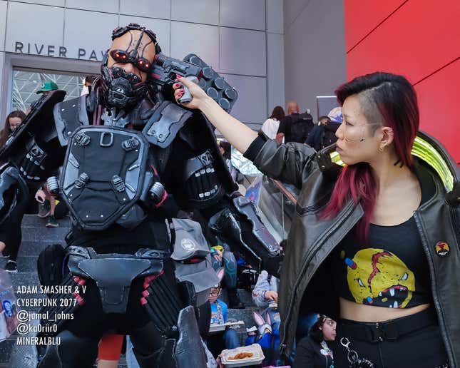 A cosplayer dressed as V from Cyberpunk 2077 holds a gun to the head of a cosplayer dressed as Adam Smasher.