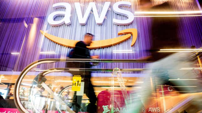 A man steps onto a conference venue escalator with a giant AWS logo in the background