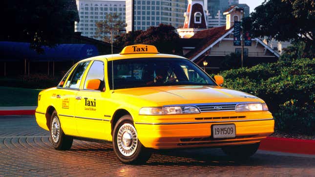 A photo of an old Ford Crown Vic taxi cab parked at a traffic circle. 