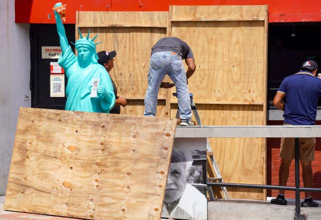 People board up store windows and doors with sheets of plywood