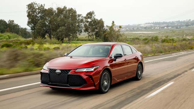 Une Toyota Avalon rouge circulant devant un champ 