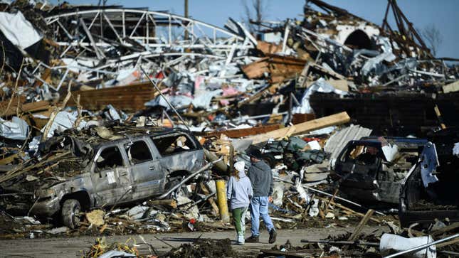 Two people walking through a scene of wreckage tied to tornado damage on December 12, 2021, in Mayfield, Kentucky.