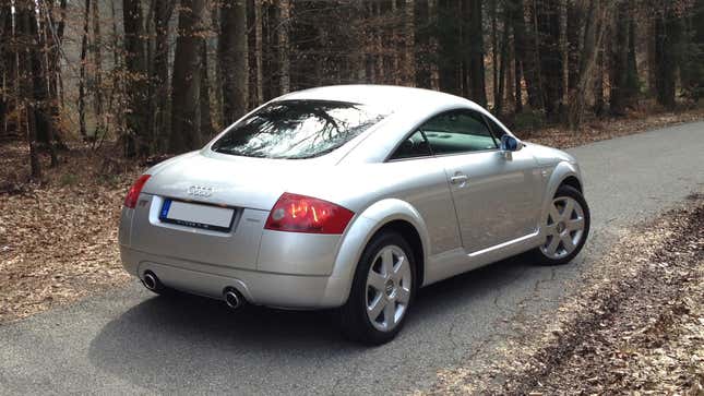 A silver 2000 Audi TT from the rear 3/4 view parked on a forest road