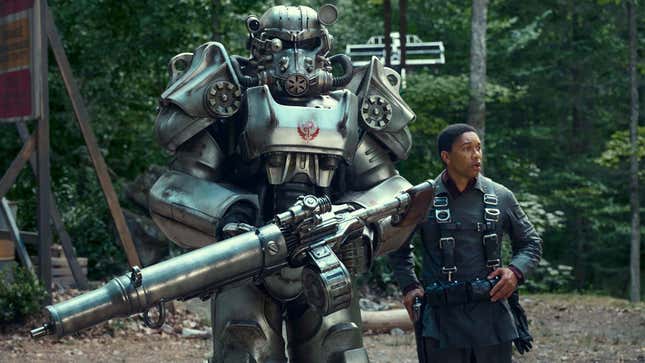 An image shows a Fallout soldier in power armor standing next to a person in the woods. 
