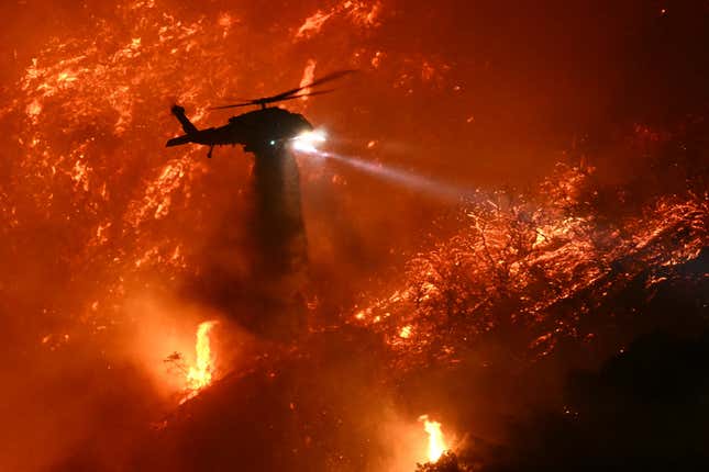 A fire fighting helicopter drops water as the Palisades fire grows near the Mandeville Canyon neighborhood and Encino, California, on January 11, 2025. 