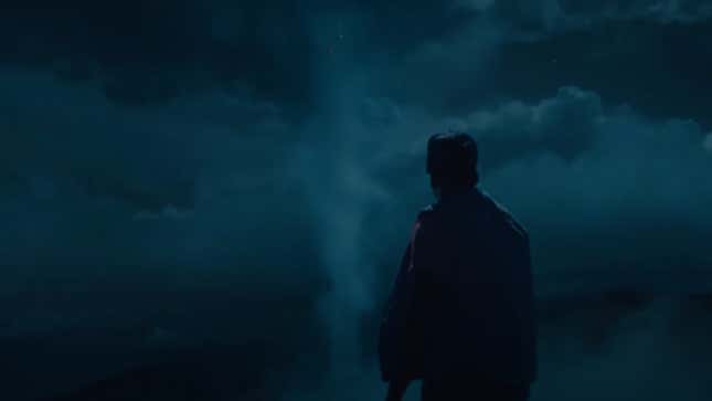 A man in a baseball cap watches an unnatural column of clouds rise into the night sky.