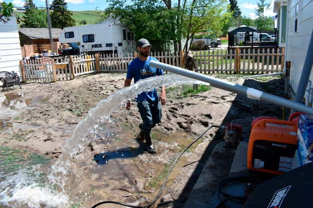 Micah Hoffman is seen in his mud-covered yard as a pump removes water  from his basement, Tuesday June 14, 2022, in Red Lodge, Mont.
