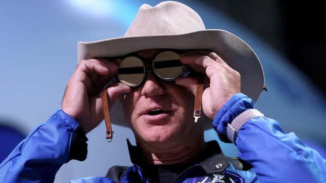 Amazon boss Jeff Bezos holding up watches to his eyes while wearing a cowboy hat at a space rocket launch. 