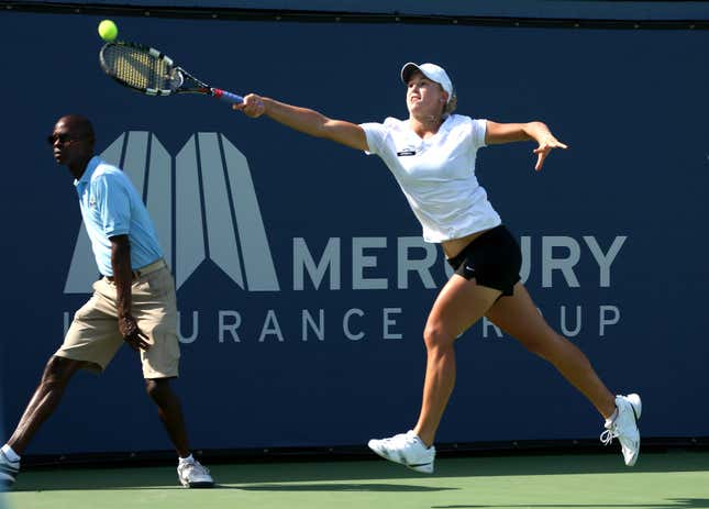 A woman playing tennis lunching for the ball in front of a Mercury Insurance Group sign