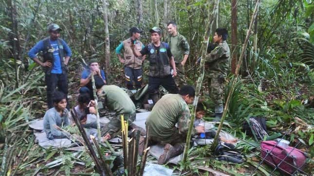 Four children sit on emergency blankets while surrounded by their rescuers. 