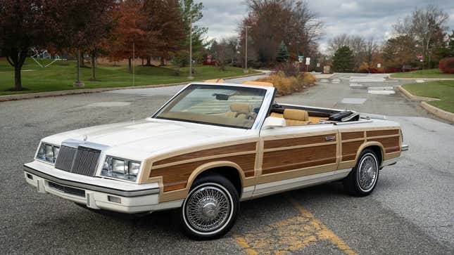 Un Chrysler LeBaron convertible en color blanco con paneles de madera estacionado en una calle