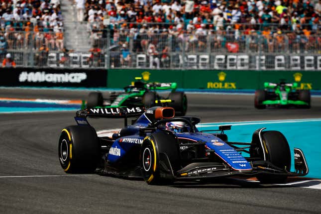 logan sargeant's blue f1 car turning a corner with two green F1 cars behind him