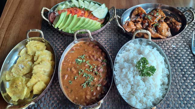 five metal trays containing beans, rice, chicken, avocados, tomatoes, and tostones