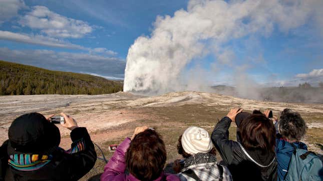 Tourists photograph Old Faithful erupting on schedule late in the afternoon in Yellowstone National Park, Wyo