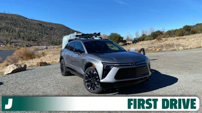 A dark grey Chevy Blazer EV parked in front of a mountain lake with a roof rack.