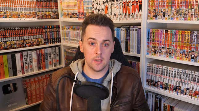 Mark of Totally Not Mark speaks into a microphone in front of bookshelves filled with manga. 