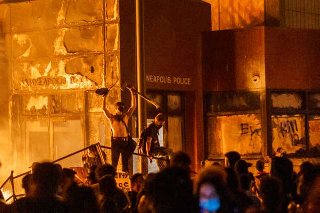 Flames from a nearby fire illuminate protesters standing on a barricade in front of the Third Police Precinct on May 28, 2020 in Minneapolis, Minnesota, during a protest over the death of George Floyd, an unarmed black man, who died after a police officer kneeled on his neck for several minutes.