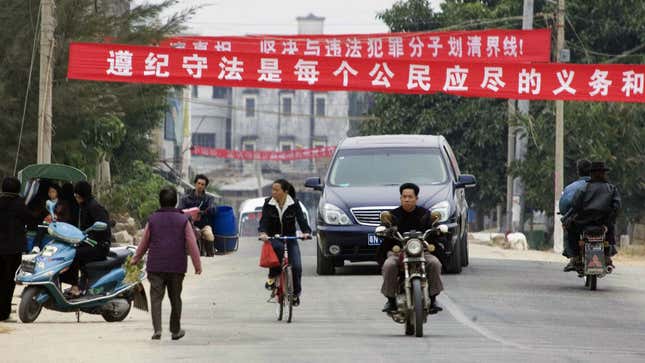 Residents pass under banners which reads "Obeying the law is every citizen's duty and responsibility" and "Recognize the truth, insist on separating from unlawful members" at the entrance to Dongzhou village near Shanwei, Guangdong, Southern China, Wednesday, Dec. 14, 2005.