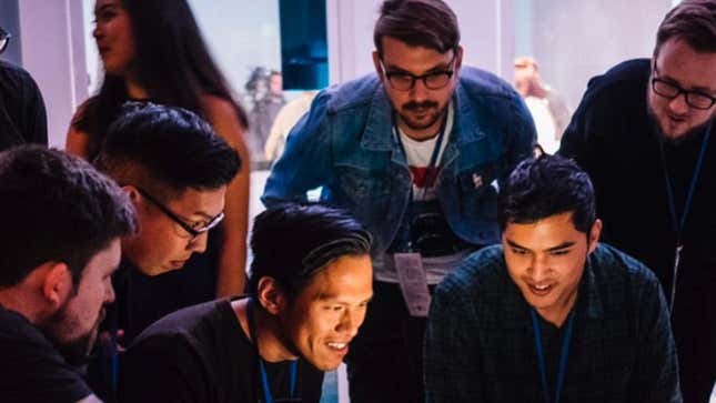 A group of guys excitedly crowd around a screen. 