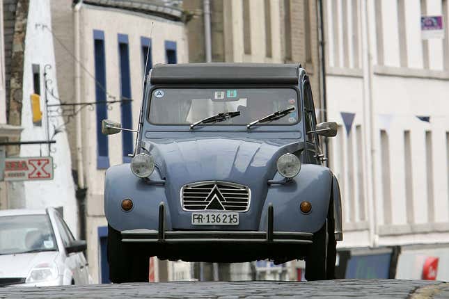 A light blue Citroën 2CV drives on a cobblestone street in Scotland.