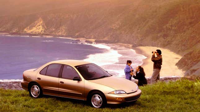 A photo of a gold Chevrolet Cavalier parked on a cliff. A man looks through binoculars behind. 