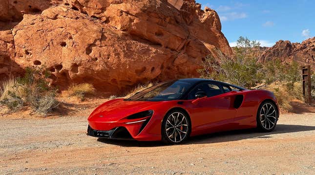 an orange 2023 McLaren Artura is parked in front of some rocks