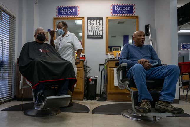 Co-owner Herbert Toliver (C) trims regular customer Pastor Blakely Scott, of First Nazareth Baptist Church, as regular customer Claude Eichelberger (R) talks politics at Toliver’s Mane Event Barber Shop in Columbia, South Carolina