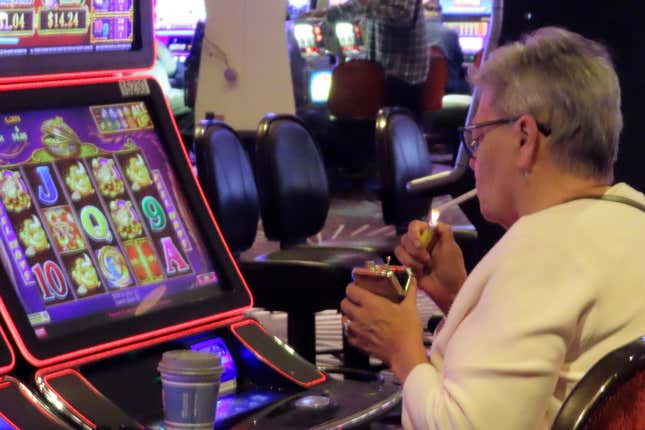 A gambler lights a cigarette at a slot machine in Harrah&#39;s casino in Atlantic City N.J. on Sept. 29, 2023. A national anti-smoking group and a Michigan health system are enlisting shareholders of major gambling companies including Boyd Gaming, Bally&#39;s, and Caesars Entertainment to push the companies to study the financial effects of eliminating smoking in their casinos. (AP Photo/Wayne Parry)