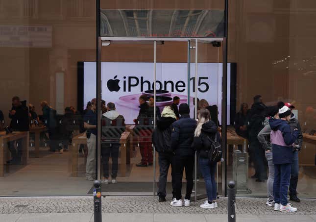 Das iPhone15-Schild im hinteren Teil eines Apple Stores ist hinter einer Menschenmenge zu sehen, die die Glasfront des Ladens betritt