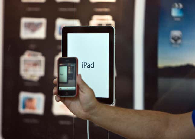 An Apple store employee holds an iPhone in front a an iPad in a window display on April 3, 2010.