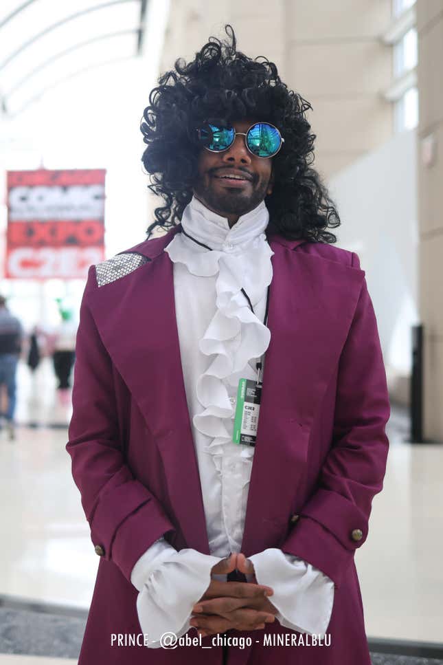 A cosplayer dressed as Prince smiles with their hands clasped. 