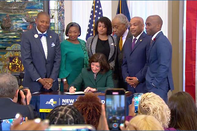 CORRECTS CITY TO NEW YORK - This image from video provided by the Office of The Governor, shows New York Gov. Kathy Hochul signing a bill in New York, Tuesday, Dec. 19, 2023, to create a commission tasked with considering reparations to address the persistent, harmful effects of slavery in the state. She is joined by, standing from left: Dr. Yohuru Williams, Founding Director of the Racial Justice Initiative at the University of St. Thomas; Andrea Stewart-Cousins, Majority Leader of the NY State Senate; Michaelle Solages, NY State Assembly Woman; Rev. Al Sharpton; Carl Heastie, Speaker of the NY State Assembly; James Sanders, NY State Senator. (Office of the Governor via AP)