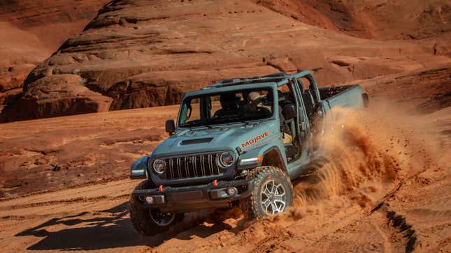 A gray gladiator driving in the sand with no doors or roof