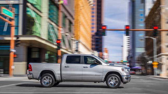 A photo of a silver Ram 1500 pickup truck driving through a city. 