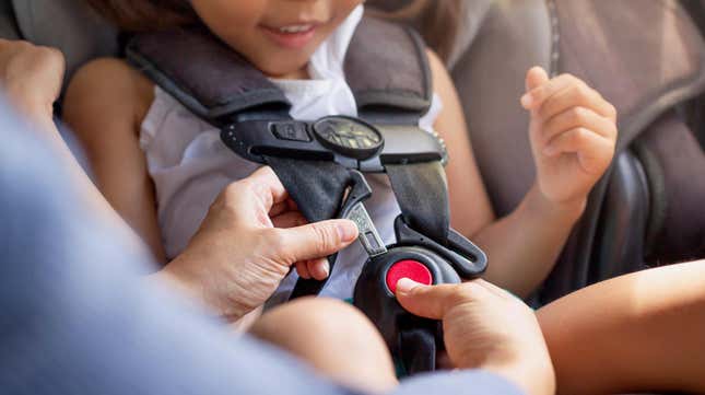 A toddler sitting in the child car seat with the mother helping to buckle and fasten seat beat properly to stay safe while driving.