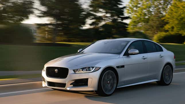 a silver Jaguar XE driving in front of trees