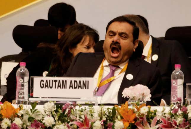 Gautam Adani at a conference table, wearing a suit and yawning