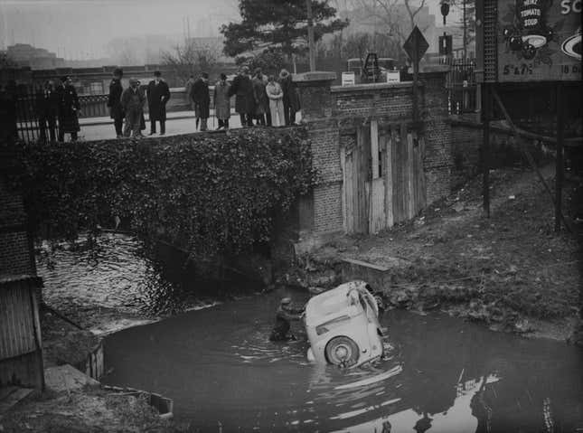 A group of passers-by looking at a car which crashed through a fence and fell 20 feet into Wealdstone Brook, London