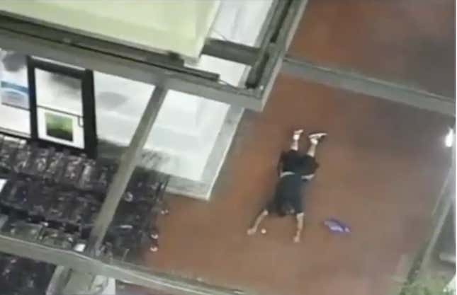 A man lies down on the sidewalk, photo taken from above outside of a grocery store.