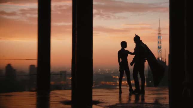 Silhouettes of Selina Kyle, aka Catwoman, and Bruce Wayne, aka Batman stand in front of Gotham City at dawn.