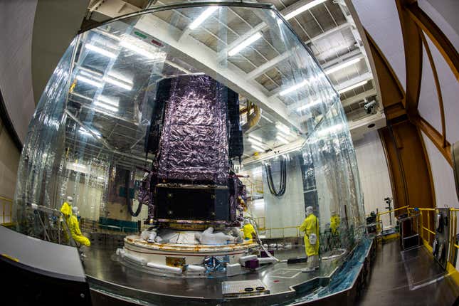 Workers wearing coveralls and masks prepare the James Webb Space Telescope for launch within a protective transparent plastic barrier