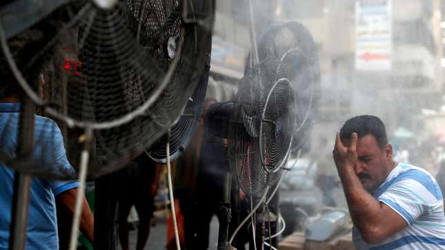 A man stands by fans spraying air mixed with water vapor deployed by donors to cool down pedestrians along a street in Iraq's capital Baghdad on June 30, 2021 amidst a severe heat wave.
