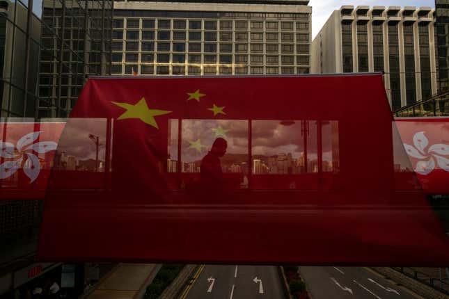 FILE- A pedestrian walks through a footbridge is silhouetted as Chinese and Hong Kong flags are strung to mark the 26th anniversary of the city&#39;s handover from Britain to China in Hong Kong, on June 27, 2023. Hong Kong’s plan to enact a new national security law, on top of a sweeping legislation that was imposed by Beijing and used to crack down on dissent, is deepening concerns over the erosion of freedoms in the former British colony.(AP Photo/Louise Delmotte, File)