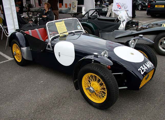 A black and yello Lotus 7 is parked in a paddock