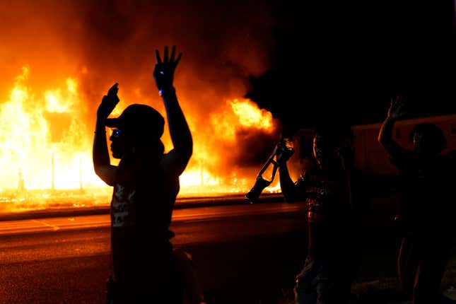 In this Aug. 24, 2020, file photo, protesters walk past police with their arms up, in Kenosha, Wis., as a building burns in the background. The federal government deliberately targeted Black Lives Matter protesters via heavy-handed criminal prosecutions in an attempt to disrupt and discourage the global movement that swept the nation last summer in the wake of the police killing of George Floyd, according to a new report released Wednesday, Aug. 18, 2021, by The Movement for Black Lives. 