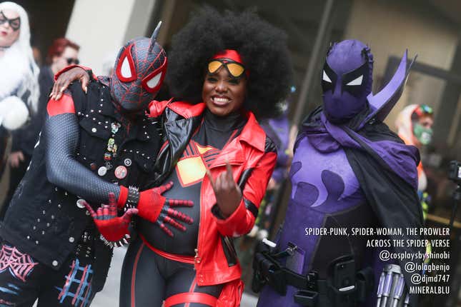 Three cosplayers dressed as Spider-Punk, Spider-Woman, and The Prowler from Across The Spider-Verse stand together, with Spider-Punk's hand on Spider-Woman's baby bump.